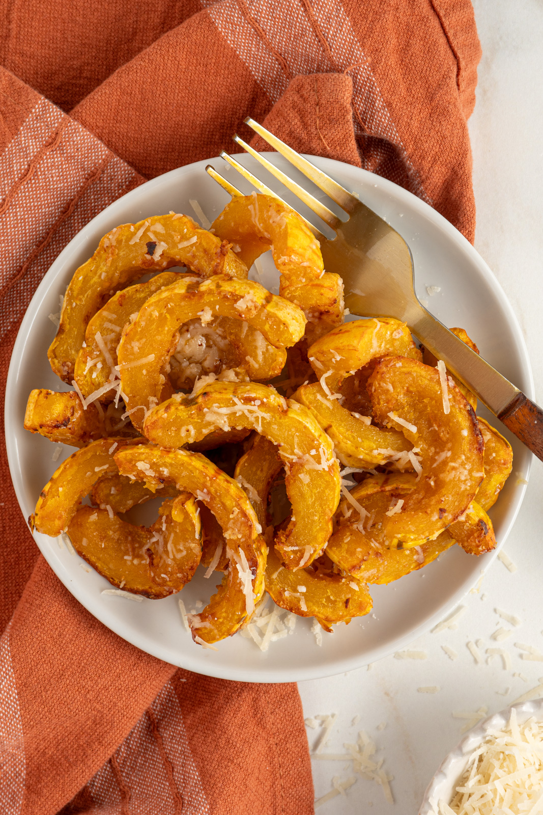 Delicata squash cooked golden brown with melted parmesan cheese on a white plate next to a fork.