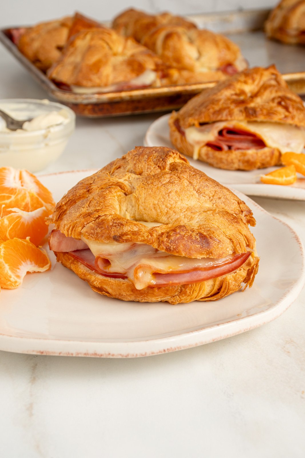 A white plate with a baked ham and cheese croissant sandwich showing sliced ham and melted cheese.