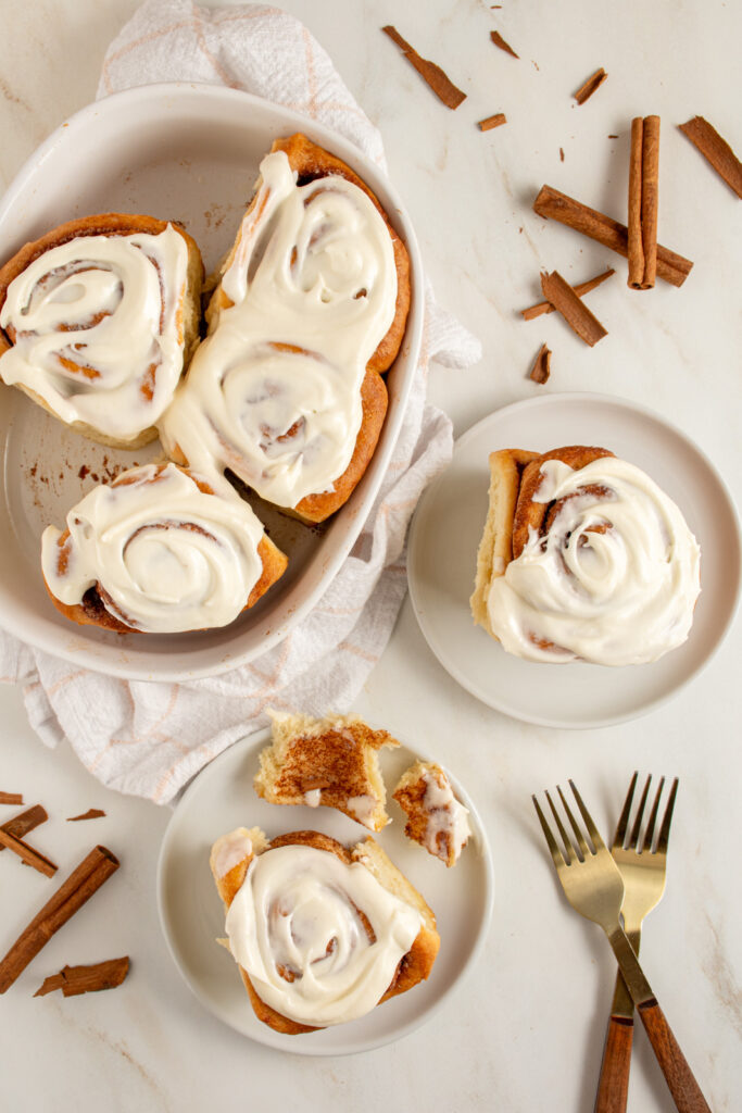 Cinnamon rolls on small plates next to a baking dish with overnight cinnamon rolls all covered in cream cheese frosting.