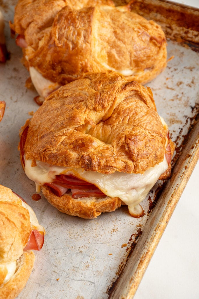 Cheese melting in a hot ham and cheese croissant and on a baking sheet.