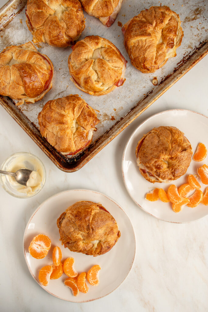 Overhead view of a sheet pan holding ham Cheese Croissants next to plates also with ham and cheese croissants for eating.