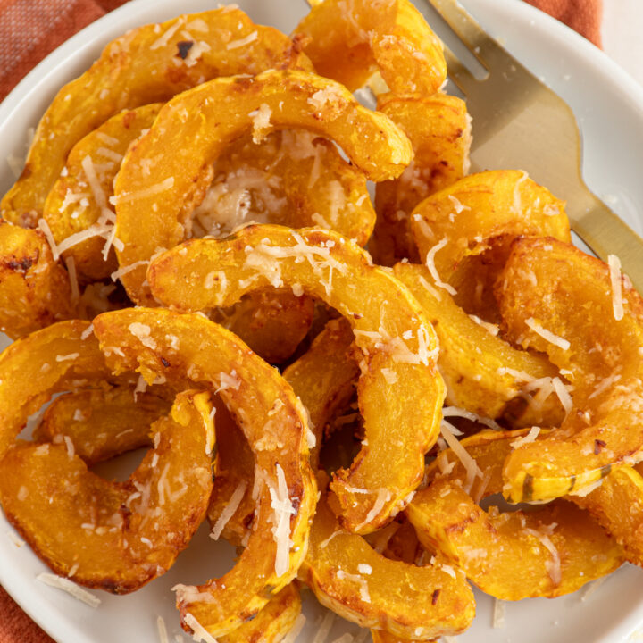 Delicata squash cooked golden brown with melted parmesan cheese on a white plate next to a fork.