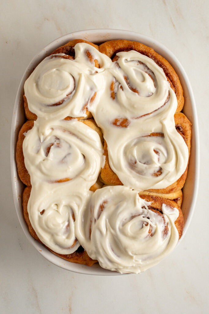 A small batch of six cinnamon rolls in a baking dish with cream cheese frosting.