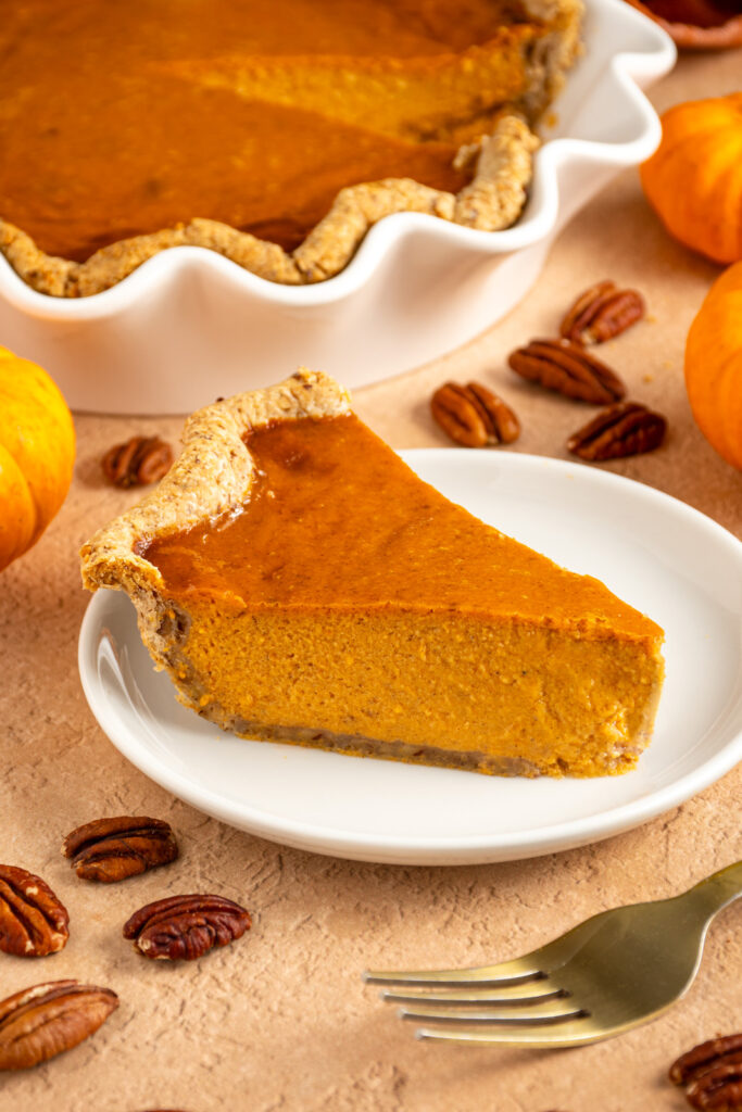 A thanksgiving pumpkin pie with pecan infused crust on a small white plate.