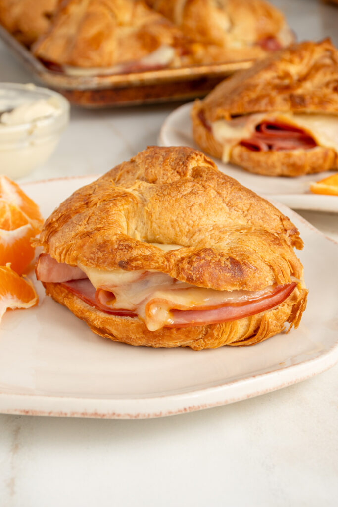A golden brown ham and cheese croissant on a white plate.