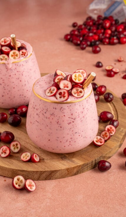 A glass filled with pink cranberry smoothie with cut cranberries on top and a straw.