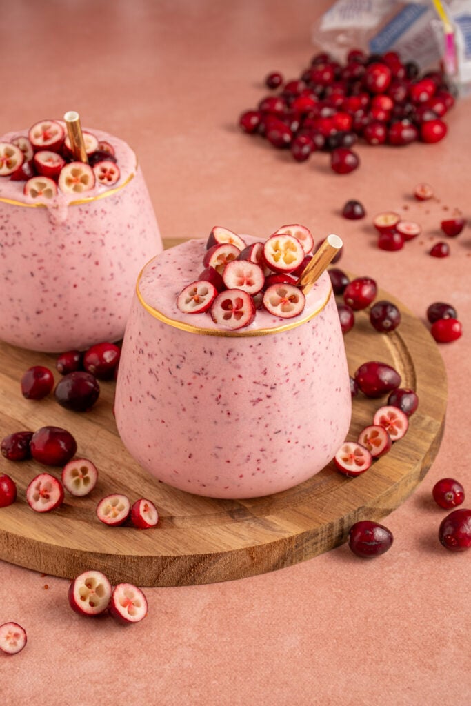 A glass filled with pink cranberry smoothie with cut cranberries on top and a straw.