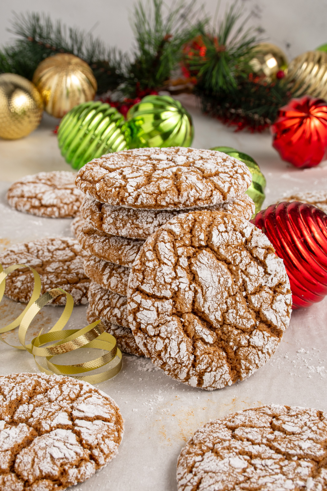 A stack of gingerbread crinkle cookies on a sheet pan with one leaning against the stack surrounded by Christmas decorations.