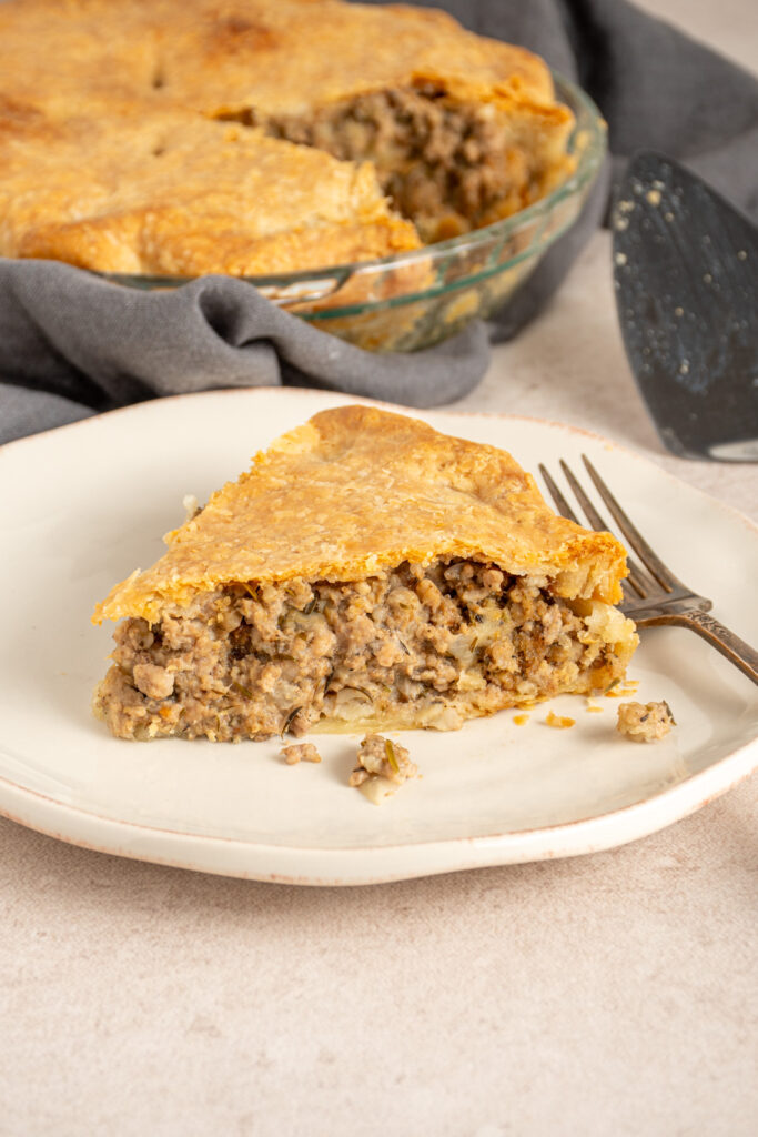 A slice of Tourtière also known as French Canadian pork pie on a white plate with meat filling and a golden flaky crust.