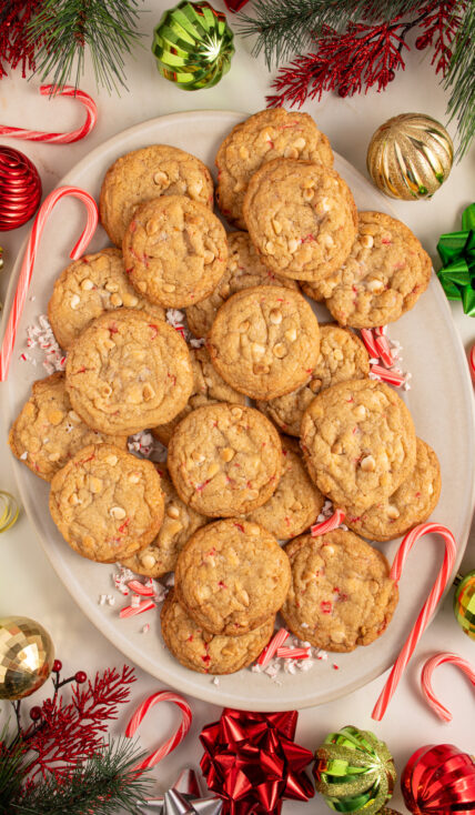 A large platter filled with white chocolate candy cane cookies with Christmas decorations all around the platter.