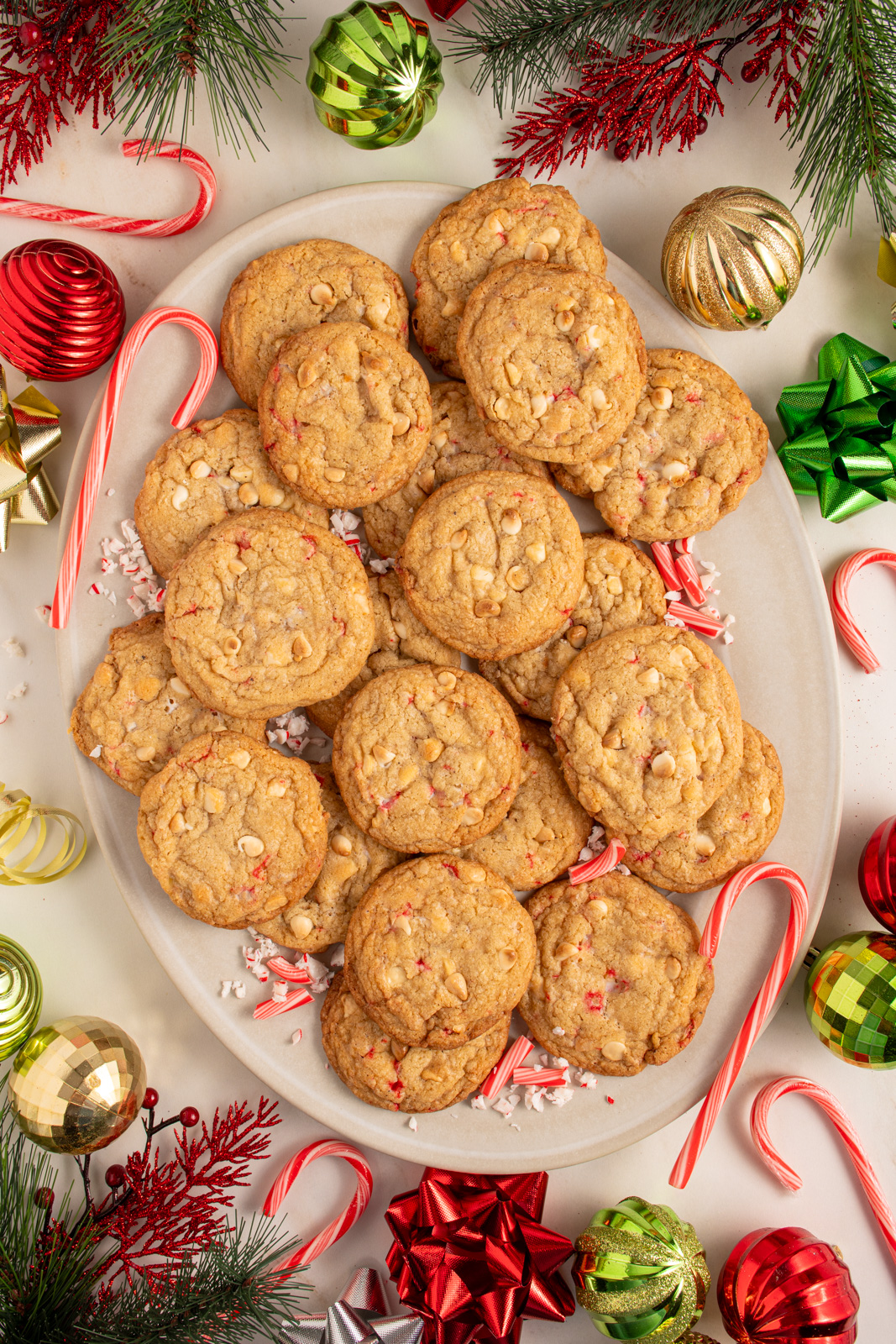 A large platter filled with white chocolate candy cane cookies with Christmas decorations all around the platter.