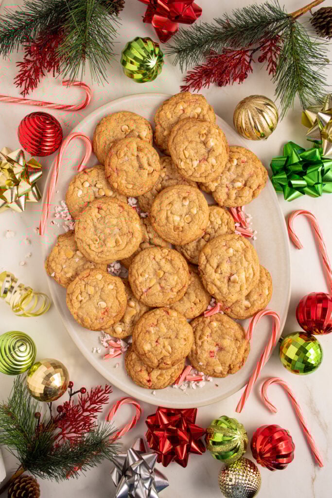 A large platter filled with white chocolate candy cane cookies with Christmas decorations all around the platter.
