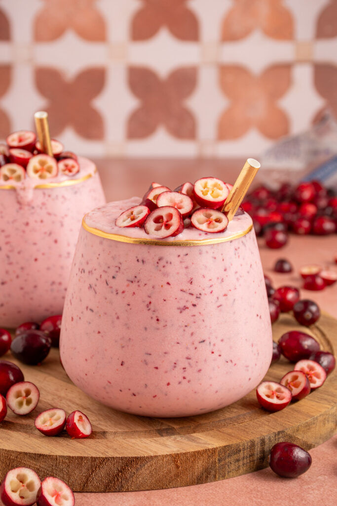 A glass filled with pink cranberry smoothie with cut cranberries on top and a straw.