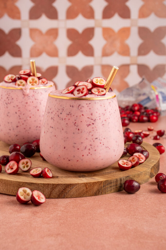 A glass filled with pink cranberry smoothie with cut cranberries on top and a straw.