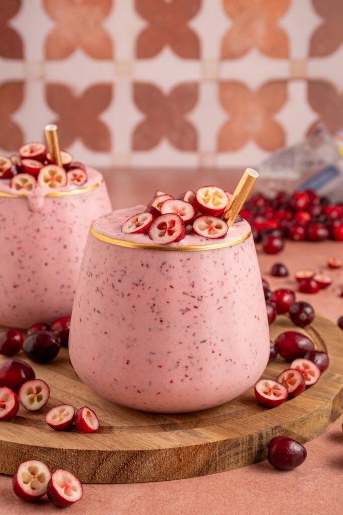 A glass filled with pink cranberry smoothie with cut cranberries on top and a straw.