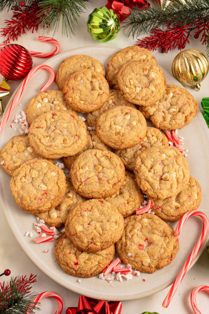 A large platter filled with white chocolate candy cane cookies with Christmas decorations all around the platter.