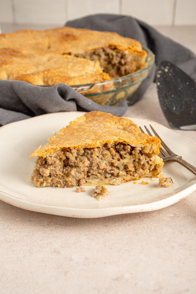 A slice of Tourtière also known as French Canadian pork pie on a white plate with meat filling and a golden flaky crust.