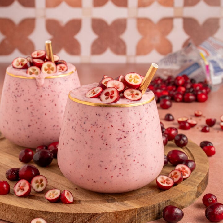 A glass filled with pink cranberry smoothie with cut cranberries on top and a straw.