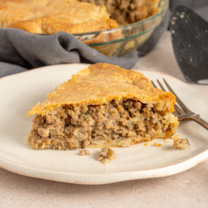 A slice of Tourtière also known as French Canadian pork pie on a white plate with meat filling and a golden flaky crust.