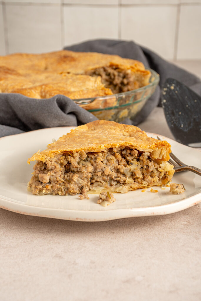 A slice of Tourtière also known as French Canadian pork pie on a white plate with meat filling and a golden flaky crust.