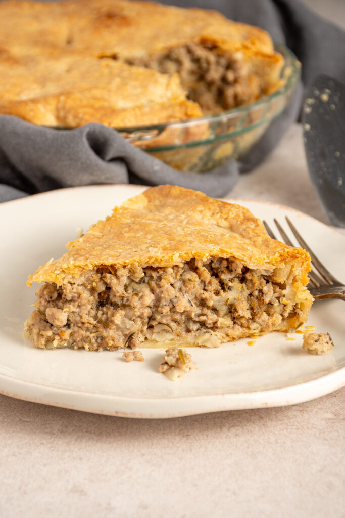 A slice of Tourtière also known as French Canadian pork pie on a white plate with meat filling and a golden flaky crust.
