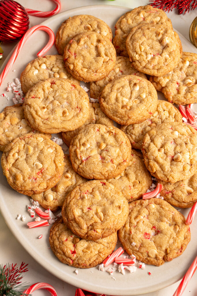 A large platter filled with white chocolate candy cane cookies with Christmas decorations all around the platter.