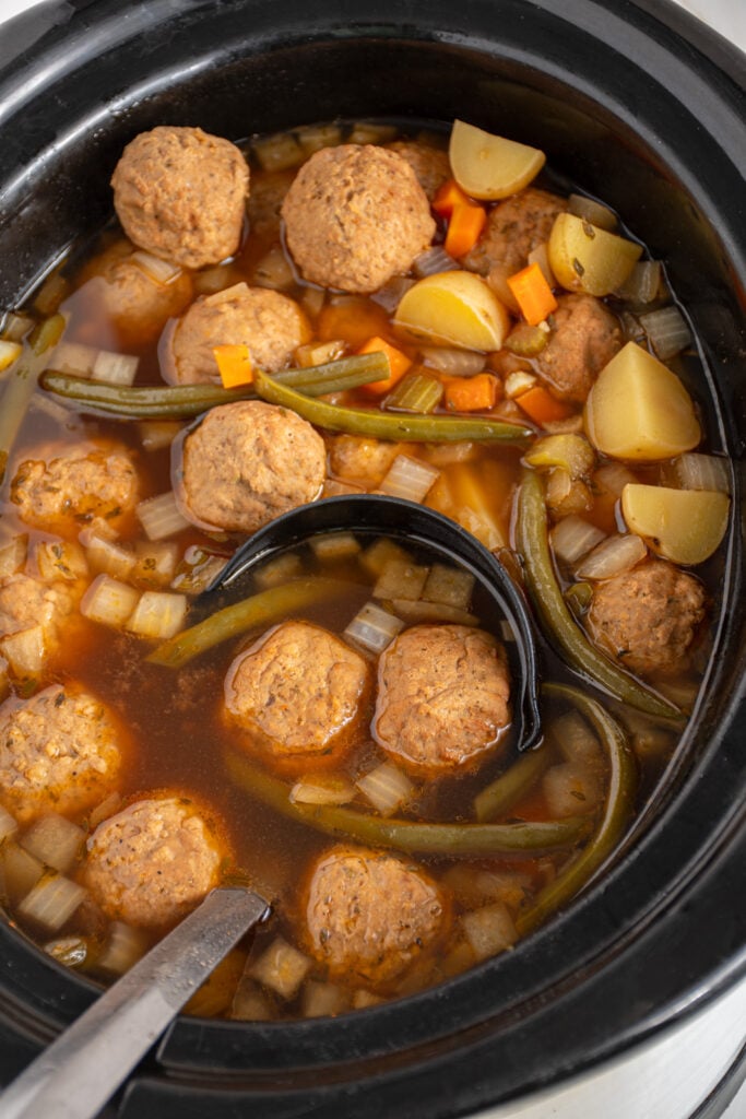 Close up of slow cooker meatball stew in a black crockpot with a black ladle.