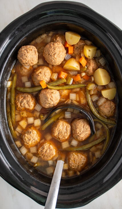 A black crockpot with a ladle filled with crockpot meatball stew.