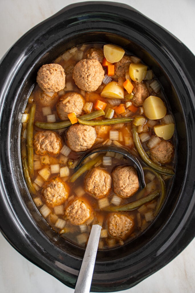 A black crockpot with a ladle filled with crockpot meatball stew.