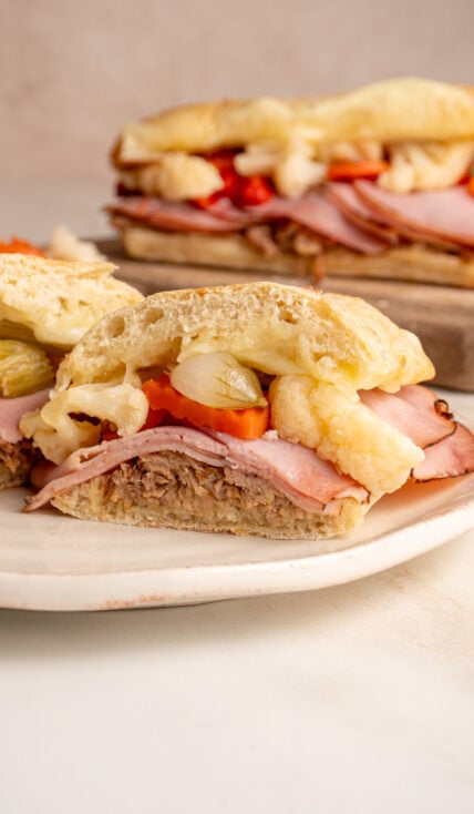 A sliced open Italian Pulled Pork Sandwich showing off pulled pork, ham, giardiniera, and provolone between a ciabatta roll.