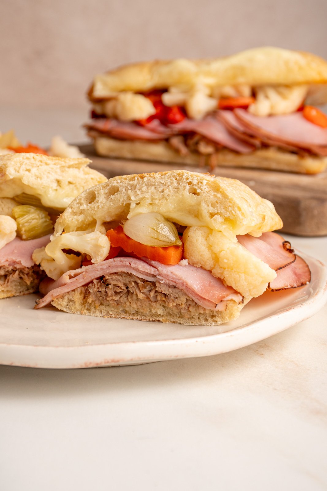 A sliced open Italian Pulled Pork Sandwich showing off pulled pork, ham, giardiniera, and provolone between a ciabatta roll.