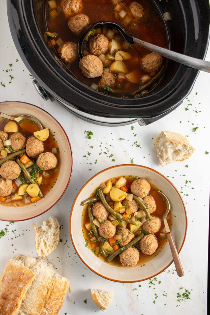 Overhead view of a crockpot and two white bowls filled with crockpot meatball stew.