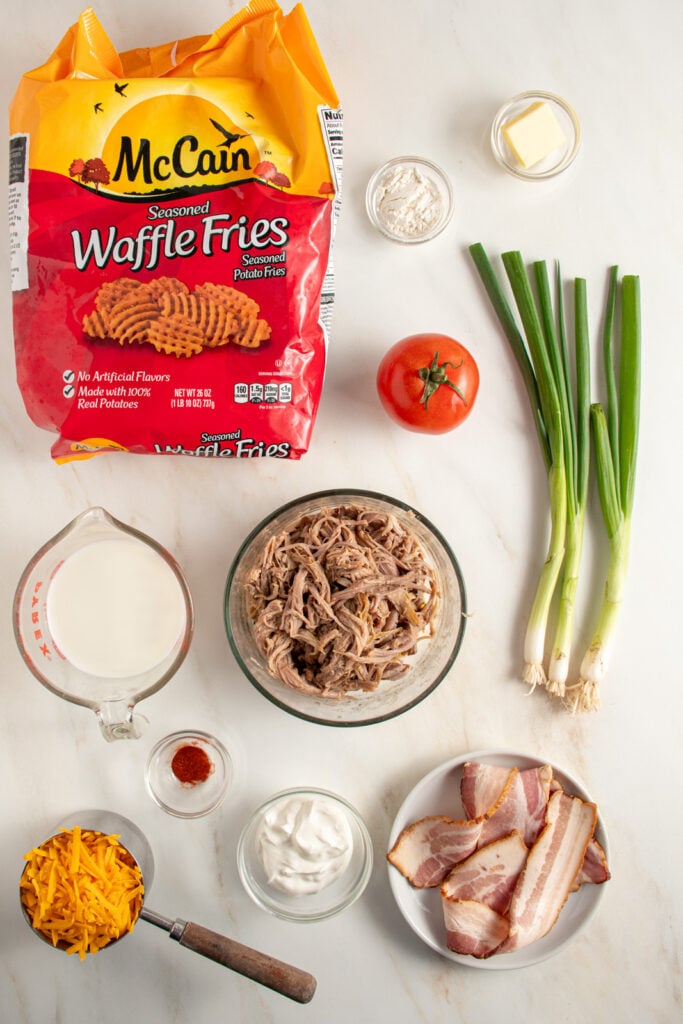 A tabletop with all of the ingredients to make pulled pork waffle fries laid out.