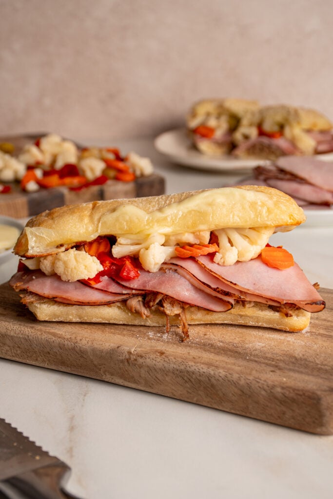 A Italian Pulled Pork Sandwich on a cutting board filled with pulled pork, ham, giardiniera, and provolone between a ciabatta roll.