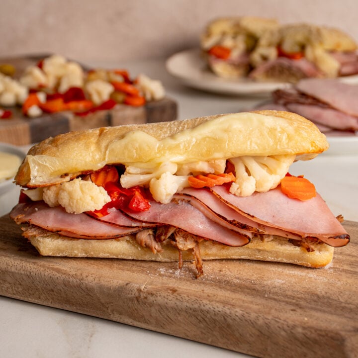 A Italian Pulled Pork Sandwich on a cutting board filled with pulled pork, ham, giardiniera, and provolone between a ciabatta roll.