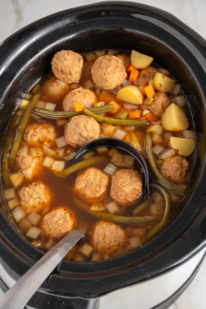 A black ladle with meatballs in a batch of slow cooker meatball stew.