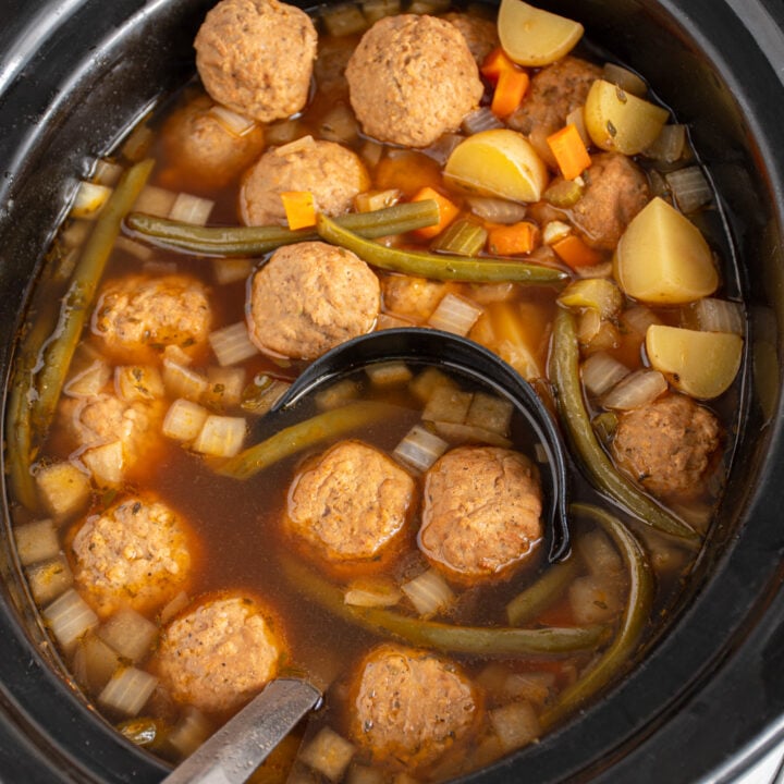 A black ladle with meatballs in a batch of slow cooker meatball stew.