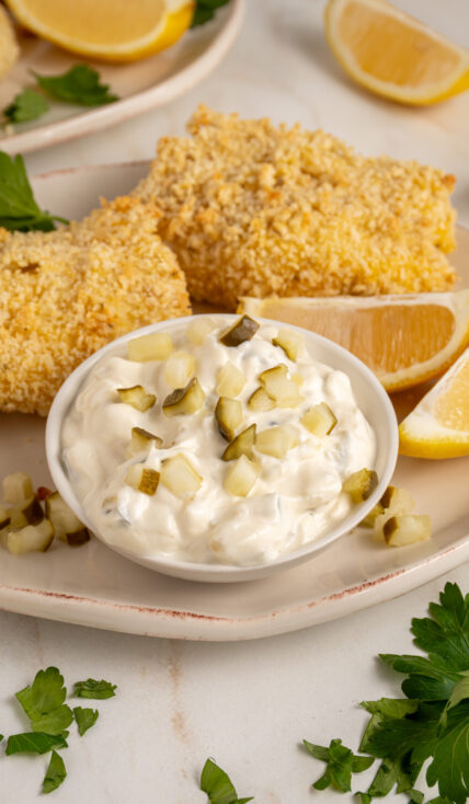 A small bowl with tartar sauce made with greek yogurt garnished with chopped pickles.