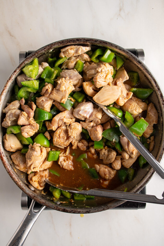 Cooking the sauce in the stir fry with chicken and bell pepper.
