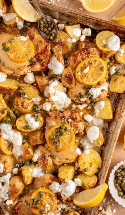 A sheet pan with balsamic chicken thighs, lemon, potatoes, and tzatziki.