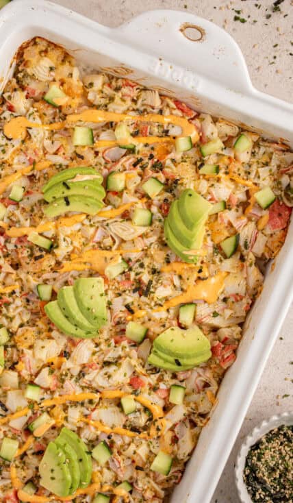 A casserole dish with shrimp and crab sushi bake garnished with avocados.