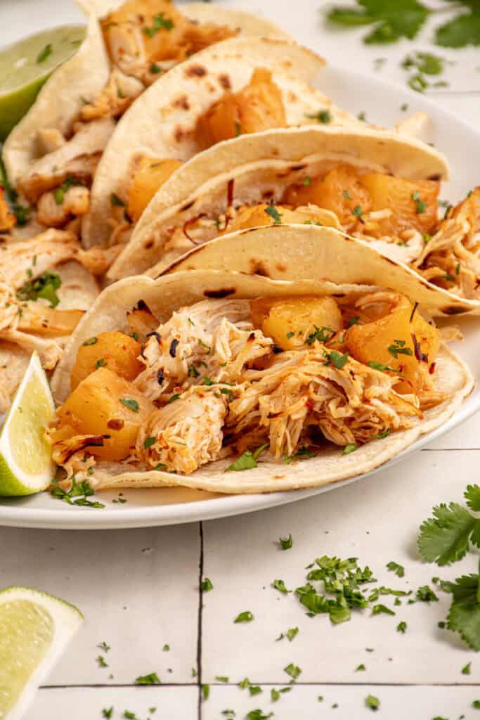 A plate with pineapple chicken tacos garnished with lime and cilantro.