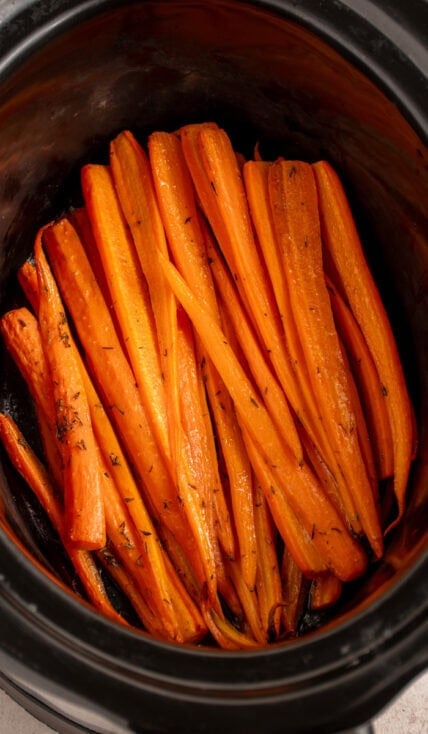 A black crockpot with cooked carrots.