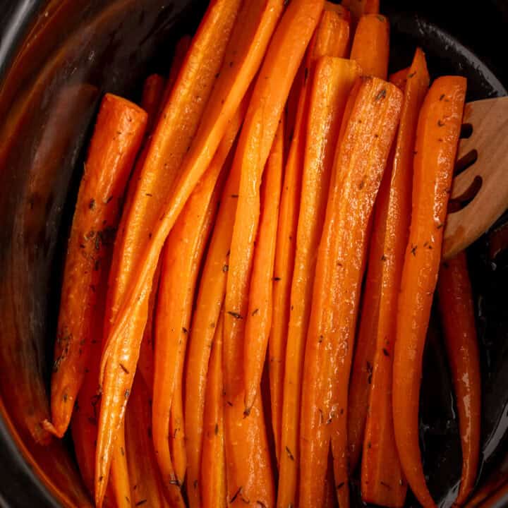 A black crockpot with cooked carrots.