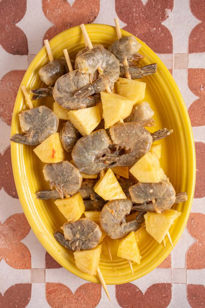 Raw shrimp and pineapple on skewers on a plate.