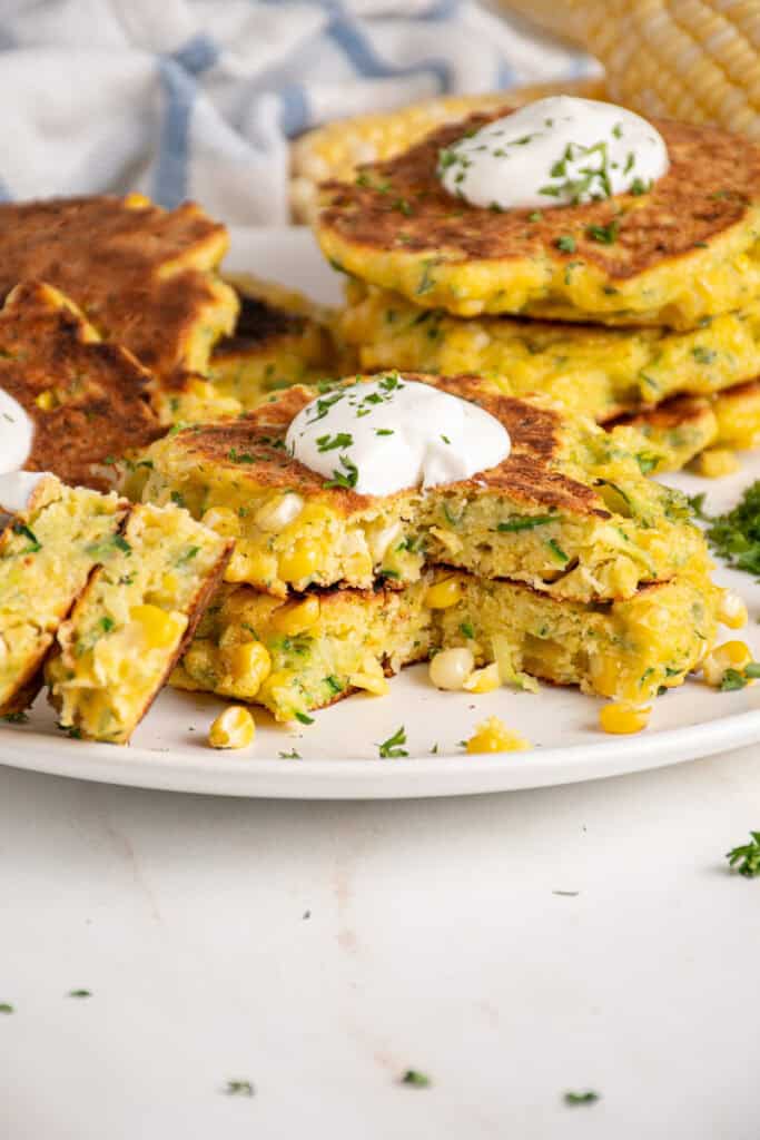 A stack of corn and zucchini fritters with a dollop of sour cream on top.