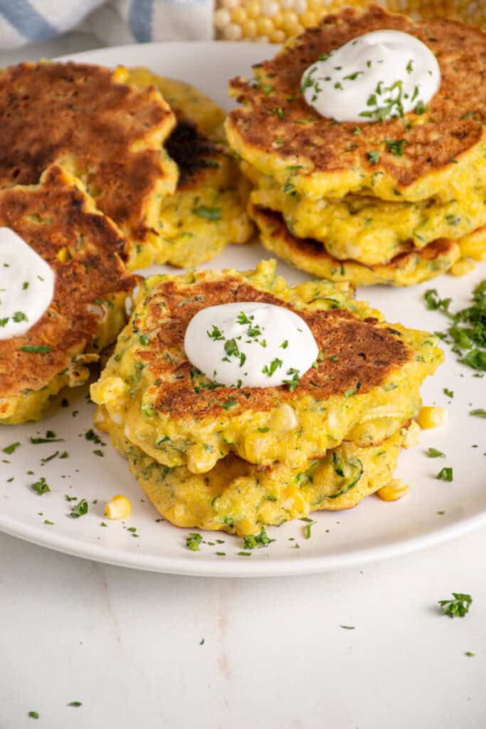 A stack of corn and zucchini fritters with a dollop of sour cream on top.