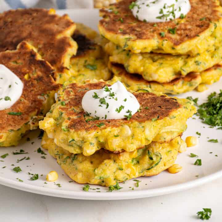 A stack of corn and zucchini fritters with a dollop of sour cream on top.