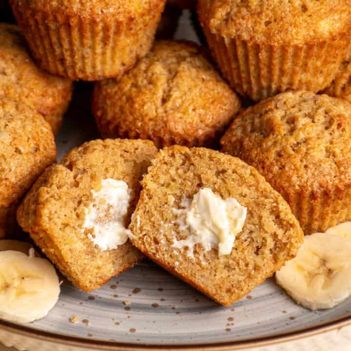 A plate filled with whole wheat banana muffins with one in the center cut in half.