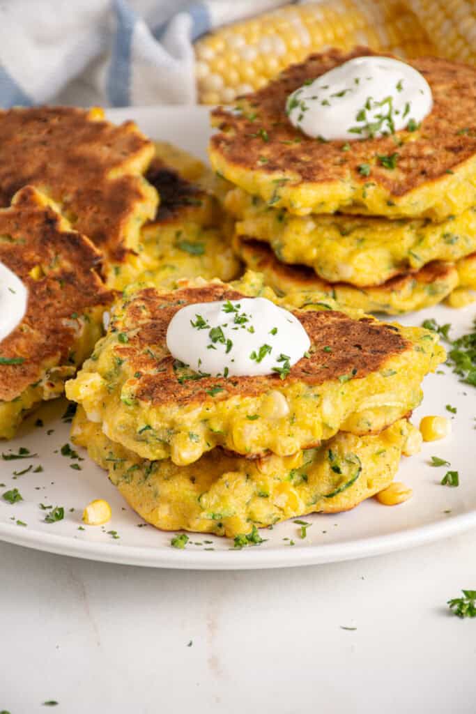A stack of corn and zucchini fritters with a dollop of sour cream on top.